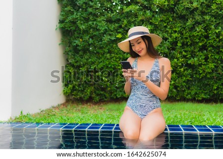 Portrait young asian woman using smart mobile phone around outdoor swimming pool in hotel resort