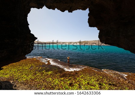 View from cave of woman in bikini exploring rugged limestone coastline on sunny day on the Great Australian Bight in South Australia