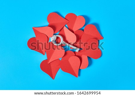 One silver vintage key on heap of red paper hearts lies on blue countertop. Concept of closed or opened love or Valentines day. Top view. Close-up