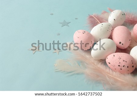 Flat lay composition easter eggs with diffrent pink feathers on blue backdrop, silver stars. Place for text. Greeting card design. Luxury decorative element. Happy Easter. Spring season.