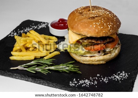 Big juicy burger with fries and sauce on a black plateau. Original feed. White background