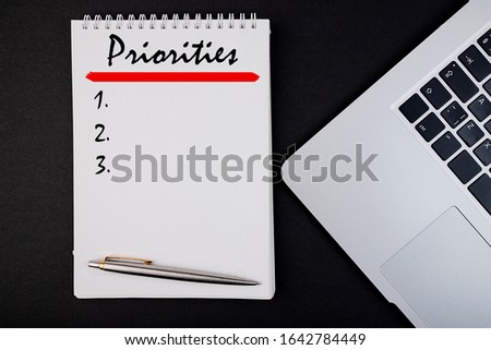 Priorities word concept written in a notebook with pen and laptop, top view.
