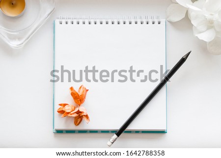 Top view open notebook, candle, pencil and flower on white desk background