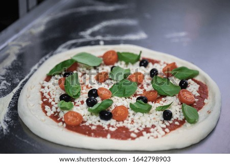 Cook in the kitchen putting the ingredients on the pizza. Pizza food concept.