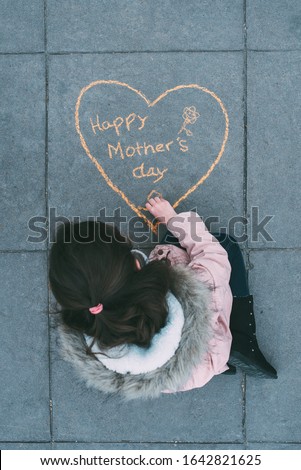 little girl painting a heart with orange chalk for mother's day. Lifestyle concept