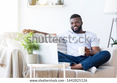 Online tv. Relaxed african american guy enjoying morning coffee and news on laptop, empty space