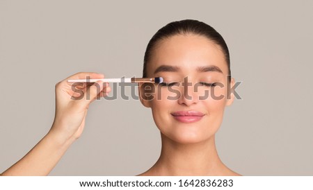 beauty concept. Makeup artist applying eyeshadows on female model face, grey background