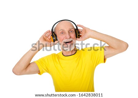 Portrait of happy, joyful senior man 70-75 years old listening to music in headphones and looking at camera with smile. Concept of lifestyle, technology, music. Isolated on white background