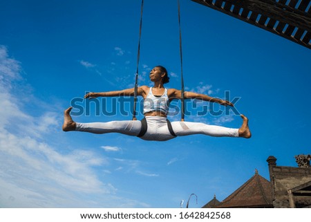 outdoors portrait of young happy and athletic Asian Indonesian woman doing aero yoga workout training body balance and relaxation hanging from swing rope in healthy lifestyle
