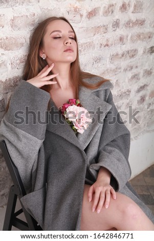 seductive portrait of a Caucasian east European fashion model wearing warm grey wool coat decorated with roses, sitting and touching her neck with closed eyes, dreaming. spring fashion concept 