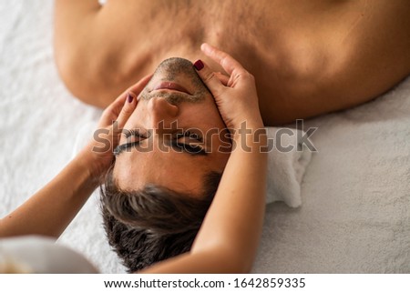 Male beauty - man receiving facial massage at luxury spa. Handsome guy, face massage. Hands of a masseuse working. Handsome man at the spa getting a facial. Man getting a massage at the healthspa Royalty-Free Stock Photo #1642859335