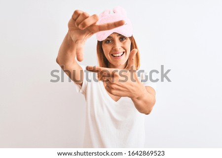 Beautiful redhead woman wearing sleeping mask over isolated background smiling making frame with hands and fingers with happy face. Creativity and photography concept.