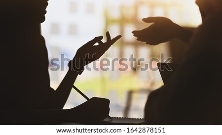 silhouette of young designer team standing with a white blank screen laptop and notebook in hands while discussing/talking about them new project with the modern office as background.