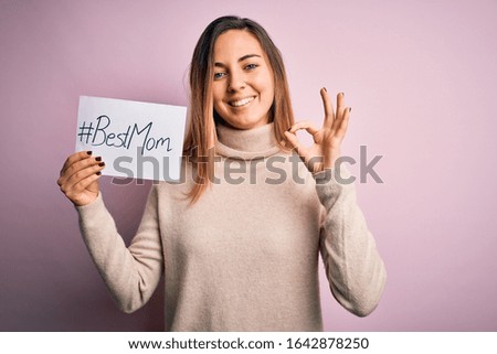 Young beautiful woman holding paper with best mom message celebrating mothers day doing ok sign with fingers, excellent symbol