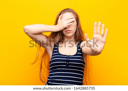 yound blonde woman covering face with hand and putting other hand up front to stop camera, refusing photos or pictures