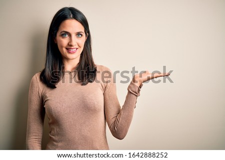 Young brunette woman with blue eyes wearing casual sweater over isolated white background smiling cheerful presenting and pointing with palm of hand looking at the camera.