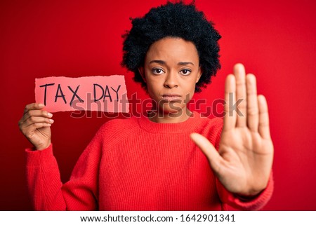 Young African American afro woman with curly hair holding paper with tax day message with open hand doing stop sign with serious and confident expression, defense gesture