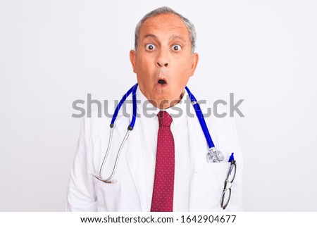 Senior grey-haired doctor man wearing stethoscope standing over isolated white background afraid and shocked with surprise expression, fear and excited face.