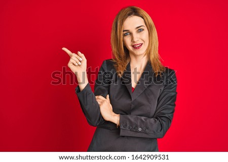 Young caucasian business woman wearing a suit over isolated red background with a big smile on face, pointing with hand and finger to the side looking at the camera.