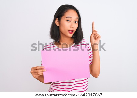 Young beautiful chinese woman holding banner standing over isolated white background surprised with an idea or question pointing finger with happy face, number one