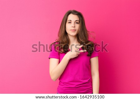 young pretty woman feeling happy, positive and successful, with hand making v shape over chest, showing victory or peace against pink wall