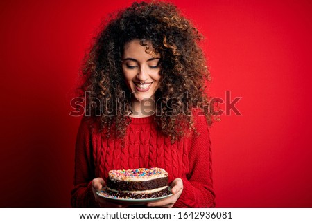 Young beautiful woman with curly hair and piercing holding plate with birthday cake with a happy face standing and smiling with a confident smile showing teeth