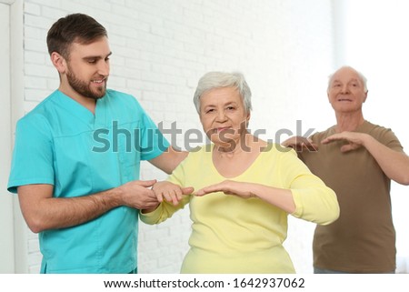 Care worker helping elderly woman to do sports exercise in hospital gym.