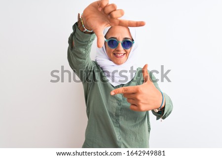 Young Arab woman wearing hijab and summer sunglasses over isolated background smiling making frame with hands and fingers with happy face. Creativity and photography concept.