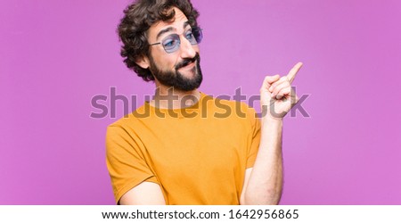 young crazy cool man smiling happily and looking sideways, wondering, thinking or having an idea against flat wall