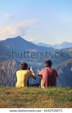 Two young people looking the mountain landscape. One of them takes a picture (vertical image)