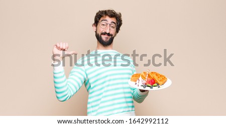 young cool man with waffles against flat wall.