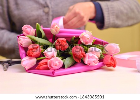 Florist hands at work making beautiful bouqet with red, pink tulips in bright pink wraper gift papper. Floral shop business concept. Beautiful flowers picture.