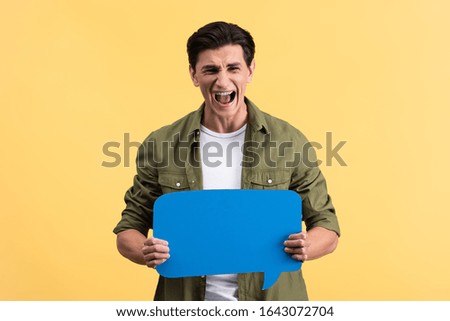 stressed man yelling and holding blue speech bubble, isolated on yellow