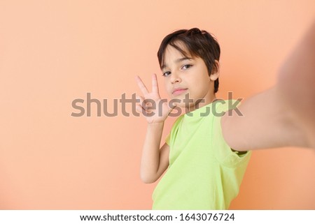 Cute little boy taking selfie on color background