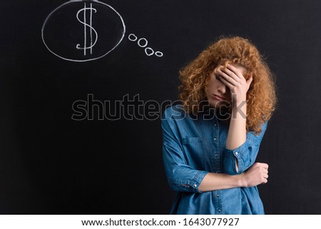upset pensive girl with dollar sign in thought bubble on chalkboard