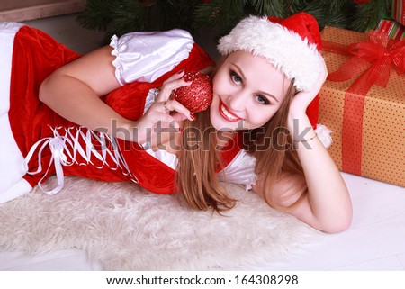 young charming girl in the Santa hat lying near a Christmas tree