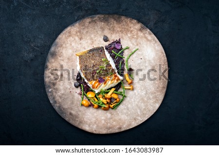 Gourmet fried European skrei cod fish filet with glasswort, fungi and algae as top view on a modern design plate with copy space 