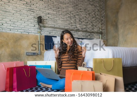 Young asian woman with smart mobile phone and laptop computer using credit card for shopping online in bedroom