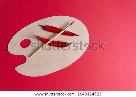 Artist brush and hot chilli peppers on wooden clean palette on red background