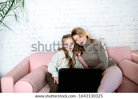 Happy mother with little kid daughter having fun online, watching video cartoons or playing game on laptop together, babysitter or nanny teaching child girl to use computer