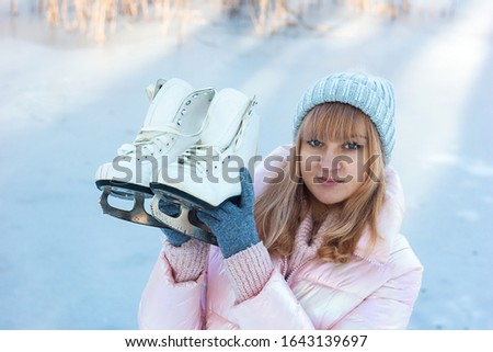 beautiful young woman in winter clothes holds curly white skates in the hands of a winter landscape, defocused portrait of a girl close-up, focus on ice skates