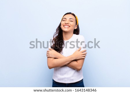 young latin pretty woman laughing happily with arms crossed, with a relaxed, positive and satisfied pose against flat wall