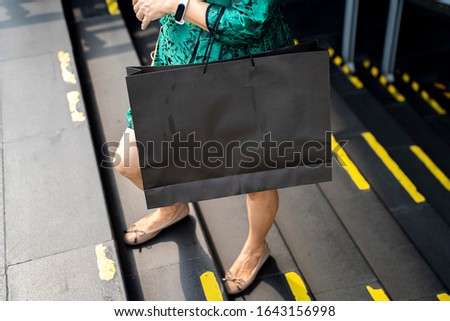 Woman holding black shopping bag with clipping path in arm and walking up stairs, Empty space on shopping bag for design insert logo or graphic for advertising, copy space