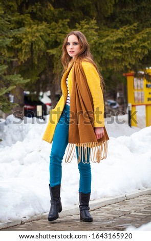 Portrait of a young beautiful teenager girl in yellow coat walking winter park
