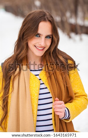 Portrait of a young beautiful girl in yellow coat posing on a background of a winter park