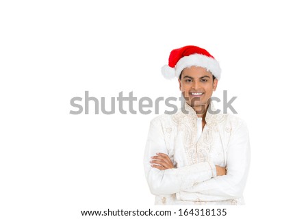 Closeup portrait of handsome smiling confident young man crossing arms in front of chest wearing red santa claus hat and dhoti, isolated on white background with space to left. Positive emotion