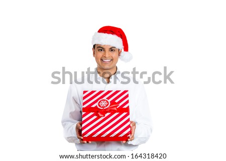 Closeup portrait of handsome smiling young man wearing red santa claus hat giving present wrapped in ribbon to you camera gesture. Positive human emotion facial expression