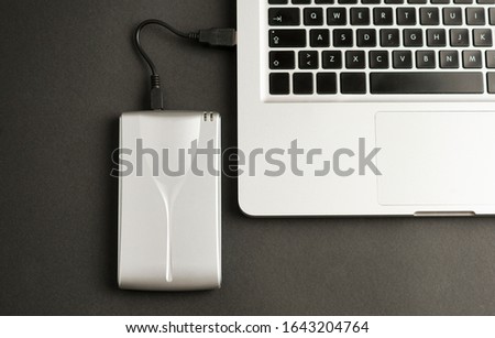 Aluminum external hard drive with clable connected to laptop, on office table, black color. Top view