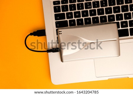 Aluminum external hard drive, partial laptop view, on orange office table.Top view