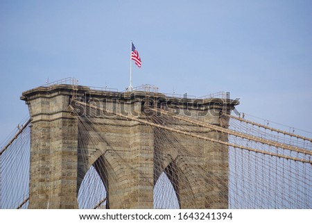 Closeup side view of the Brooklyn bridge in New York City, USA with an American flag on top of it and a blue sky in the background 